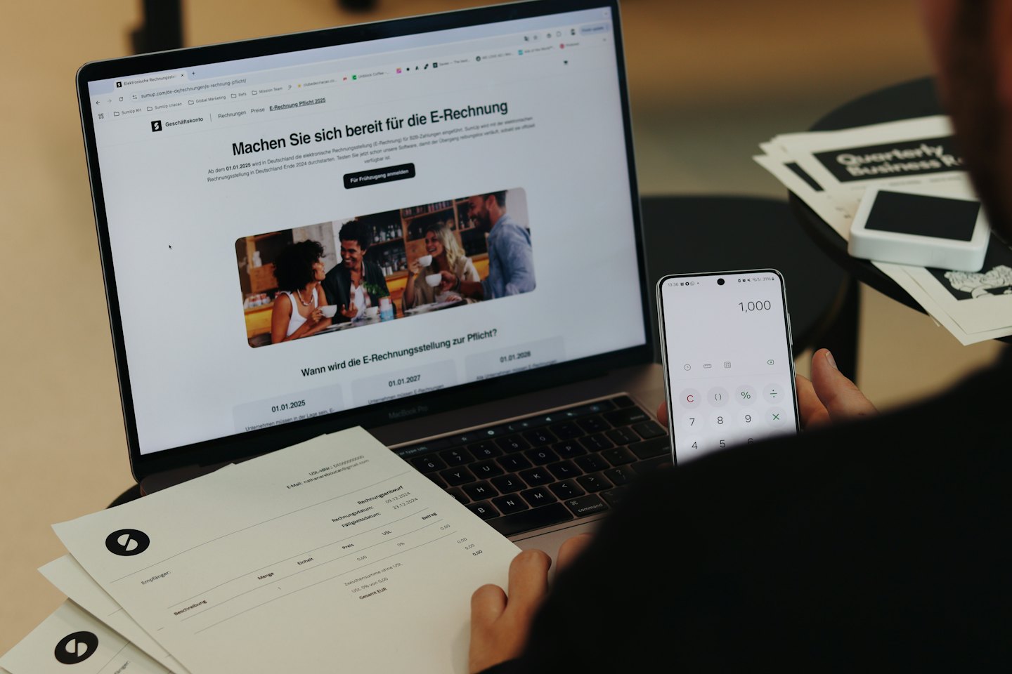 Hände halten ein Smartphone mit einem Taschenrechner neben Geschäftsberichten.